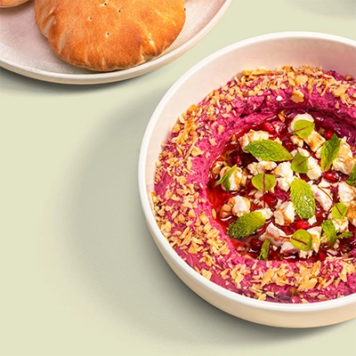 Bowl of vibrant beetroot hummus topped with nuts, pomegranate and fresh mint, served with flatbread