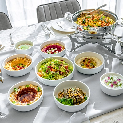 Overhead shot of an Elio catering spread with multiple mezze dishes and a chafing dish on a white table