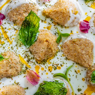 Close-up of kibbeh pieces in yoghurt sauce garnished with mint leaves, dried herbs and edible flowers