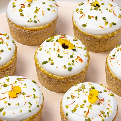 Mini tarts with white frosting topped with crushed pistachios, saffron and yellow edible flowers