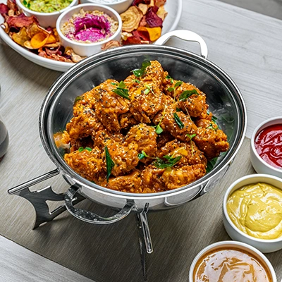 Crispy fried chicken bites in a silver chafing dish surrounded by colourful dipping sauces