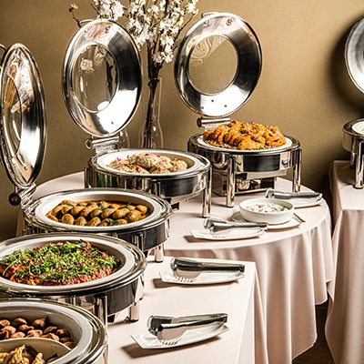 Elio catering buffet setup with silver chafing dishes filled with hot food on a white draped table